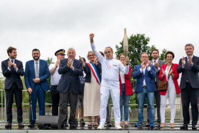 Porteur de flamme brandissant la flamme olympique sur le podium du stade du vieux moulin en compagnie d'officiels. - Agrandir l'image 10 sur 11, fenêtre modale