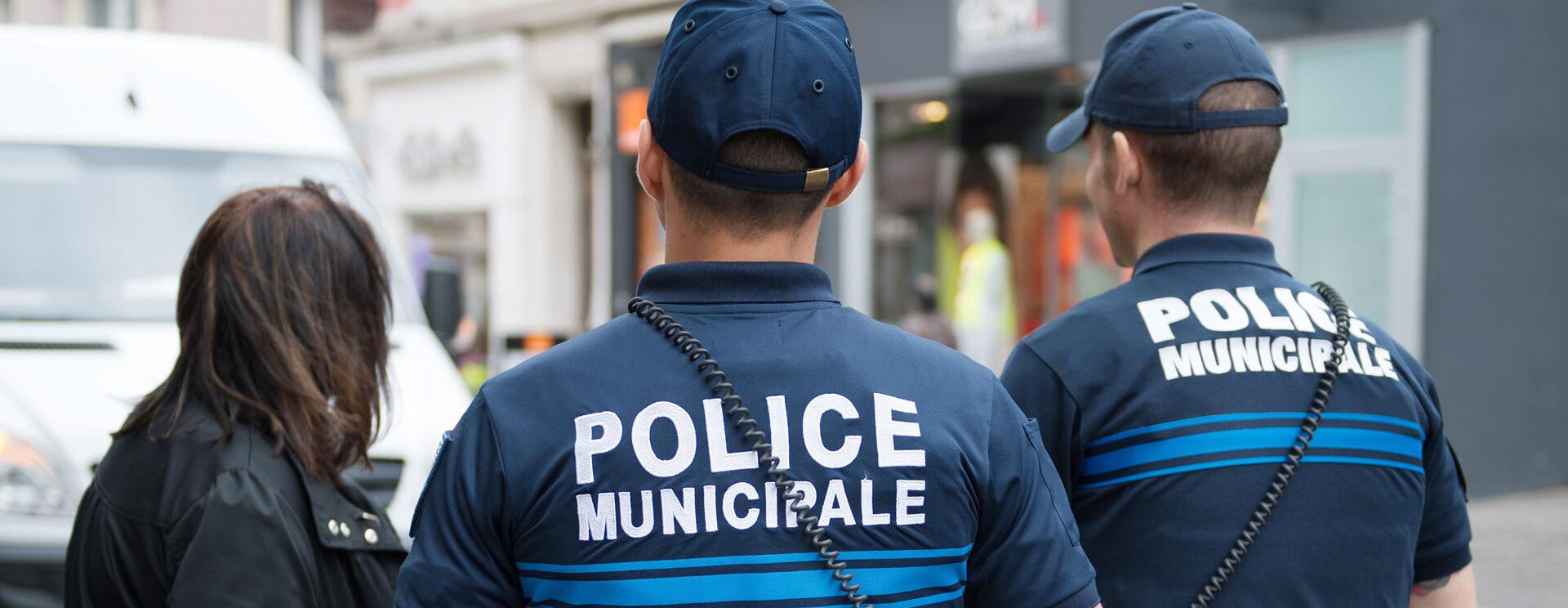 Policiers municipaux de dos en discussion avec une dame, dans un centre-ville