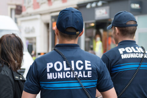 Policiers municipaux de dos en discussion avec une dame, dans un centre-ville